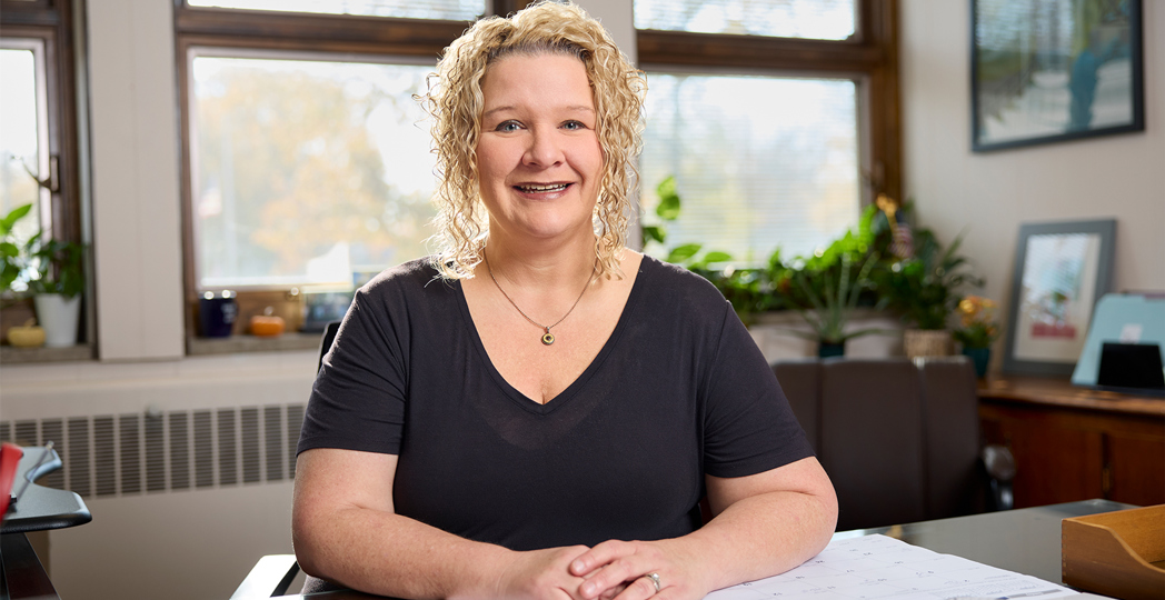 Michelle Root smiling and sitting at her desk in City Hall