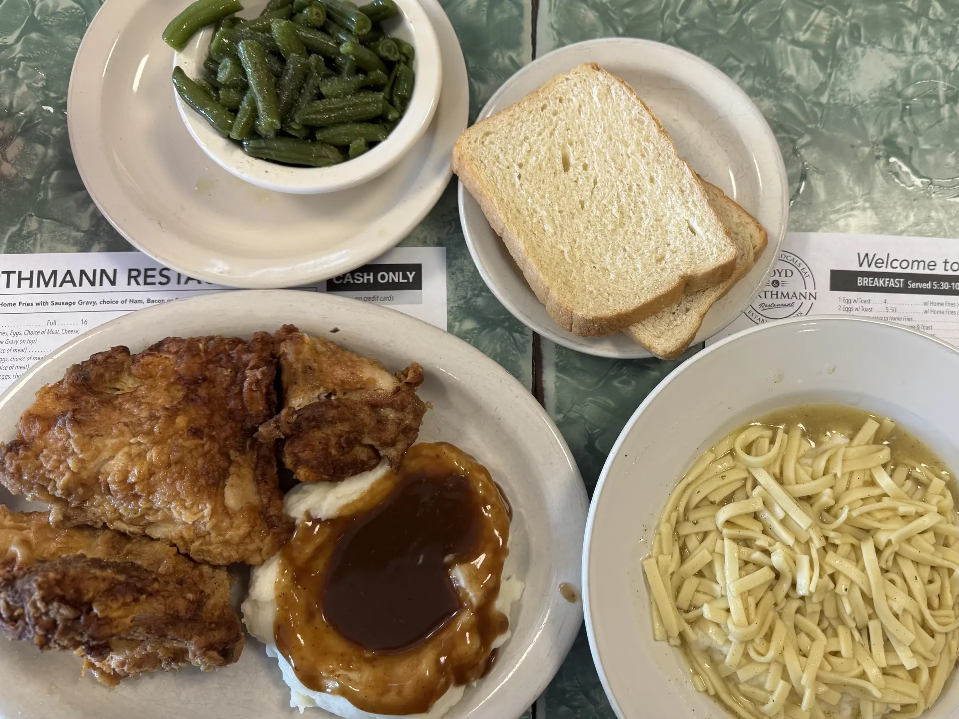 plates of fried chicken, mashed potatoes, green beans, bread, and noodles