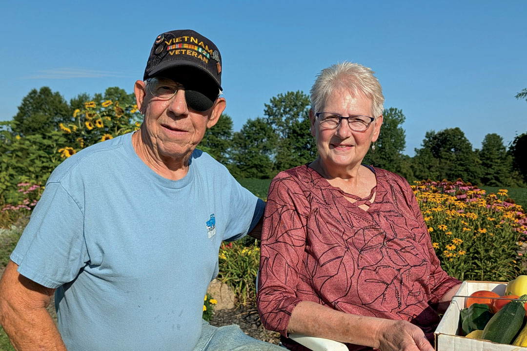 A couple smiling outside in front of a garden