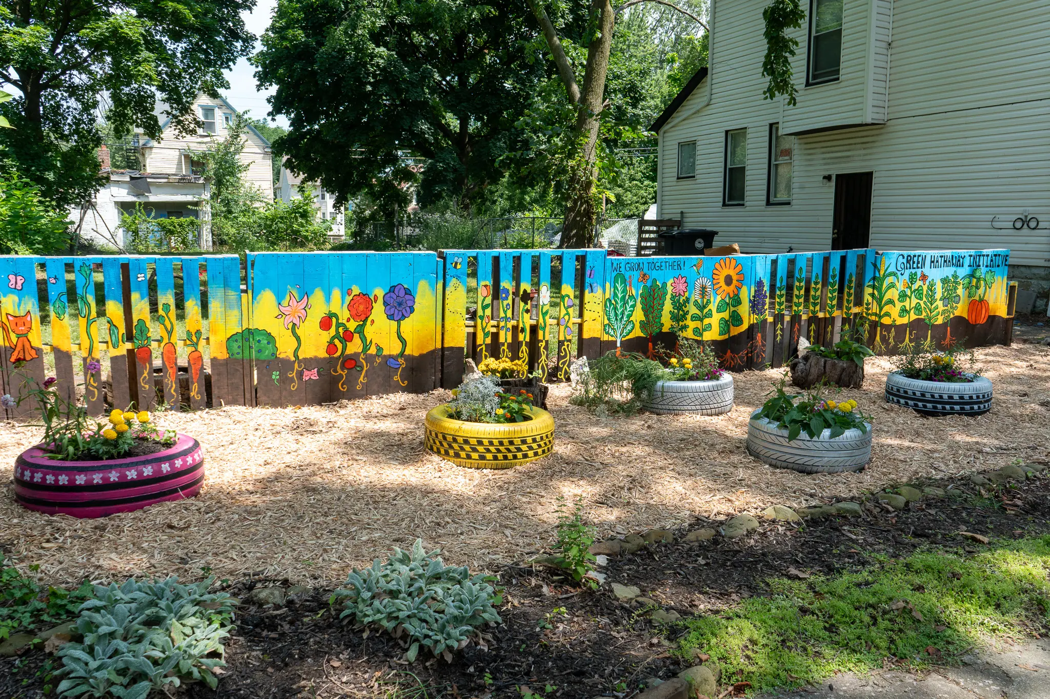 Tire beds for plants and a painted fence with mural art.