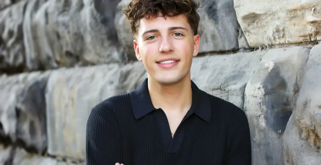a young man smiling and leaning against a brick wall