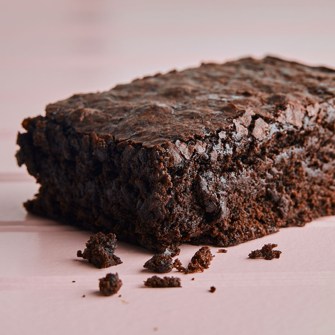 Square brownie slice on pink background.