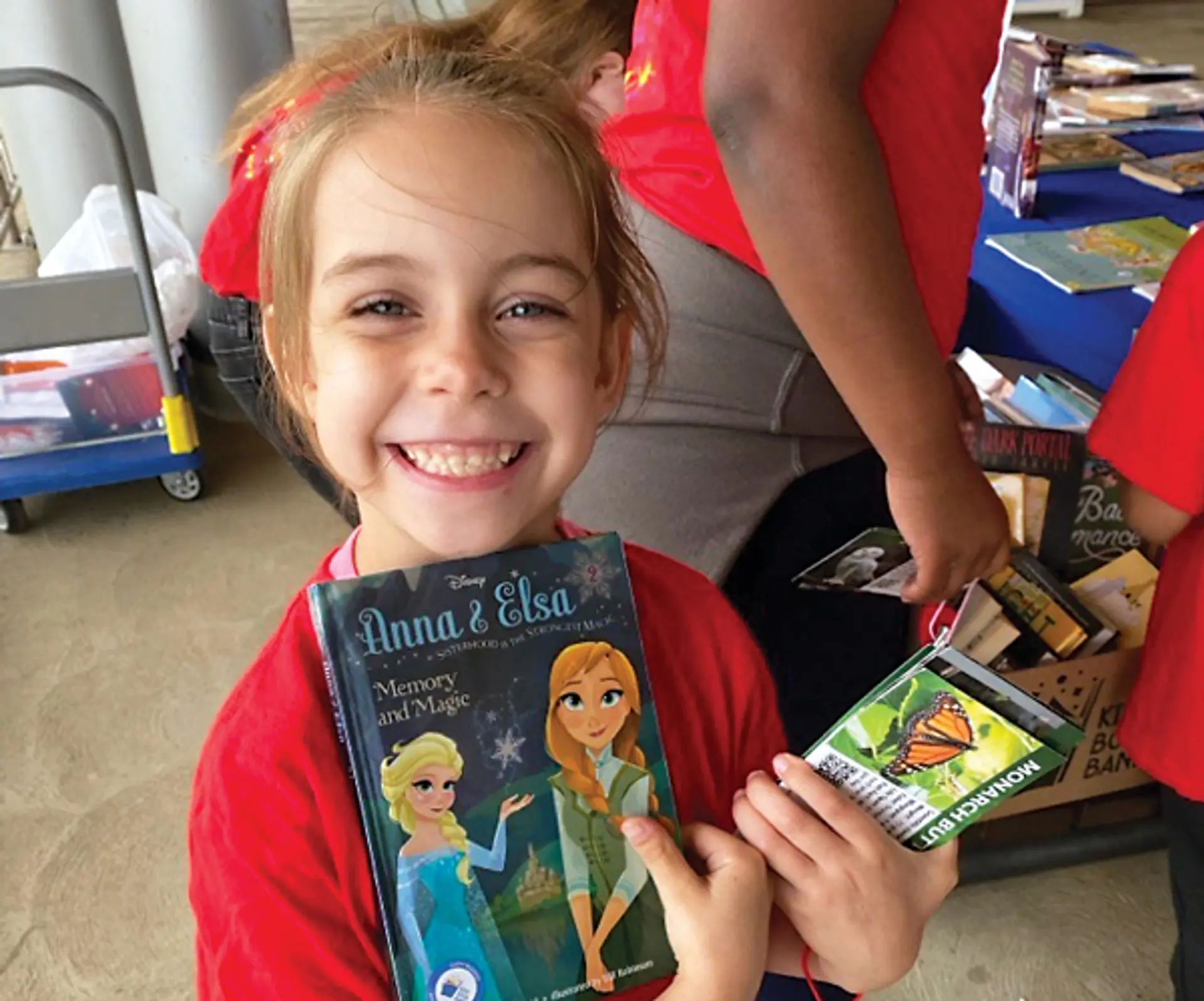 A young girl smiles and holds up two books