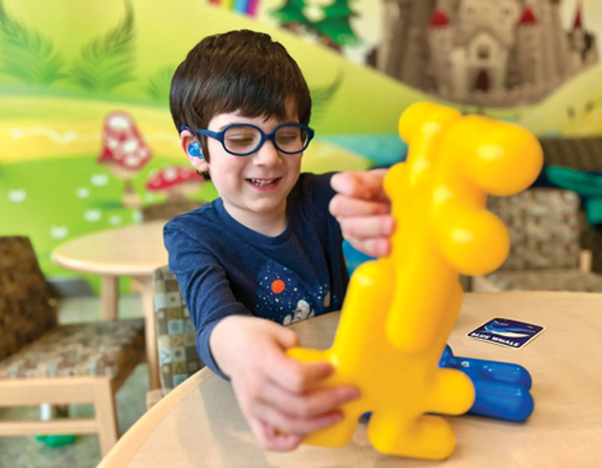 A young boy wears hearing aids and plays with a yellow toy