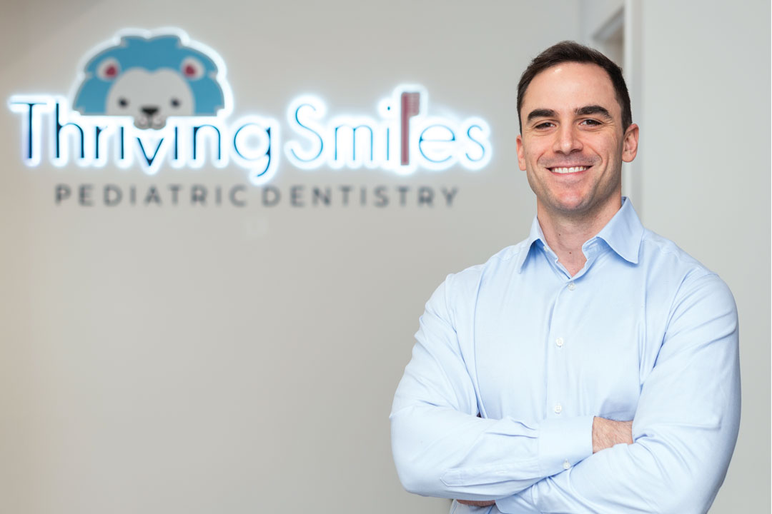 George Boukas smiling in front of the Thriving Smiles sign