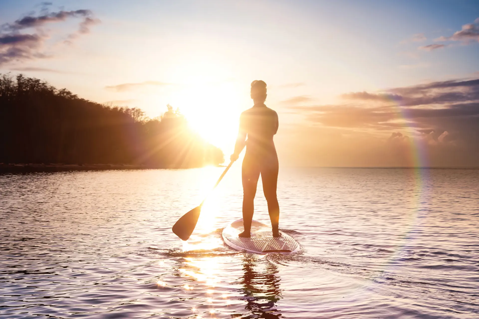 someone paddleboards in front of a sunset