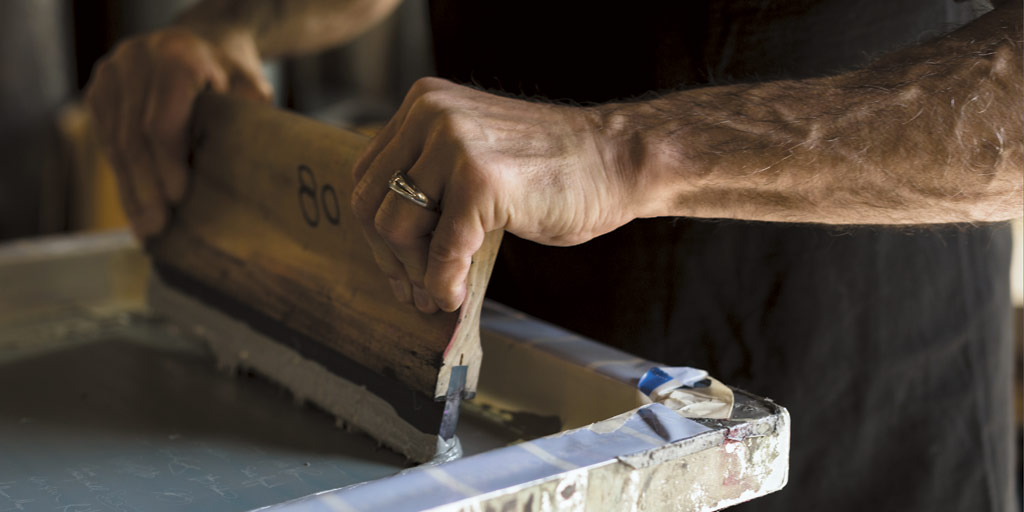 Gil Kudrin hovers over a manual screen-printing press