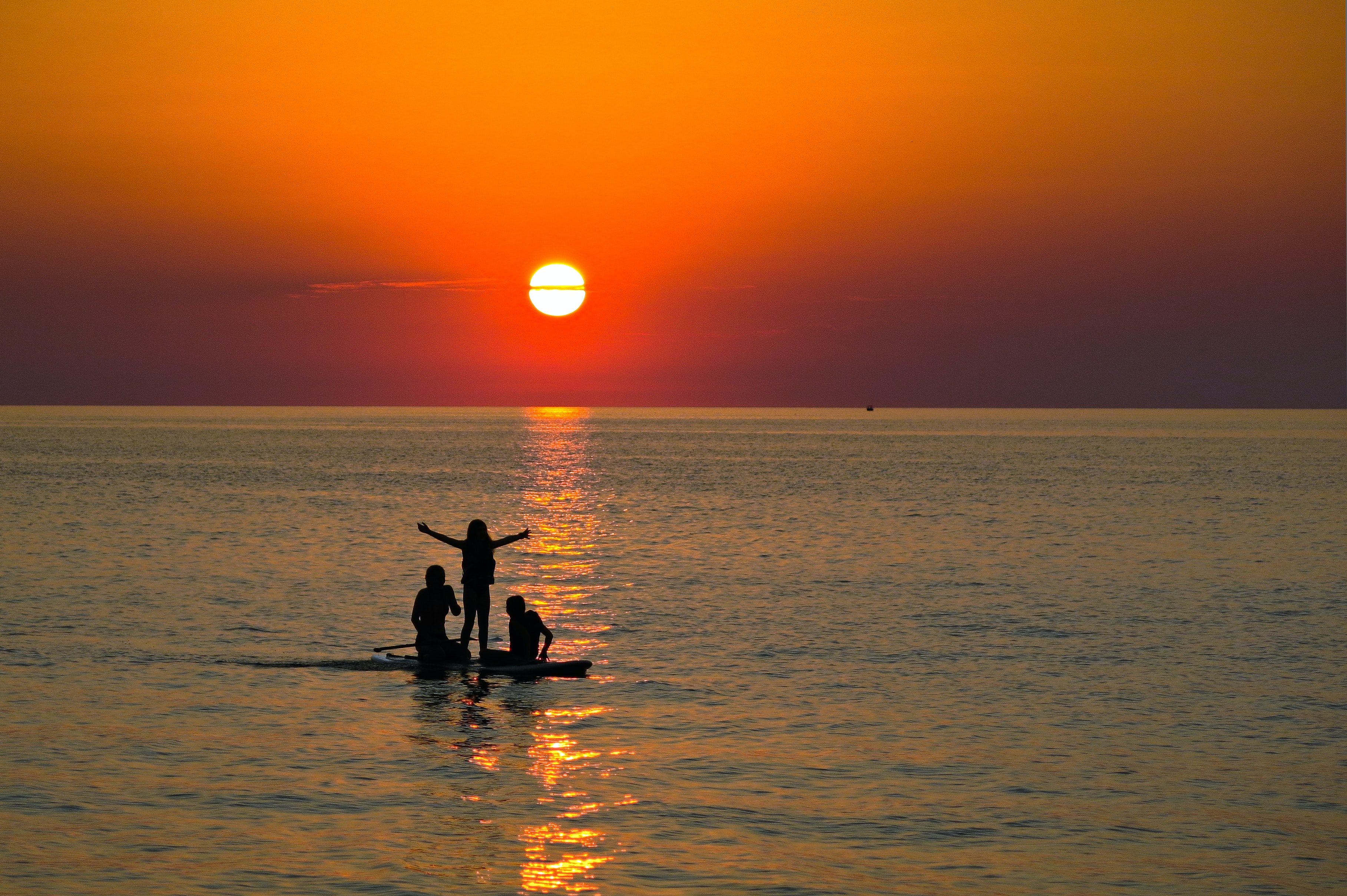 Three people on a paddle board in Lake Erie at sunset Three people on a paddle board in Lake Erie at sunset
