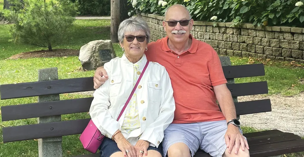 A couple smiling outside in front of a garden
