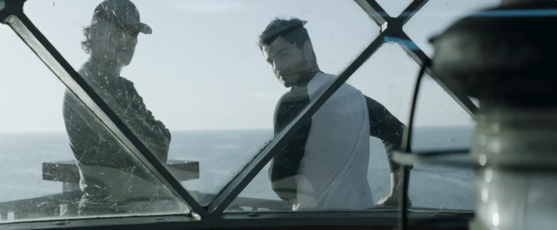 Two men look through the window of a lighthouse in Beneath The Light movie still.